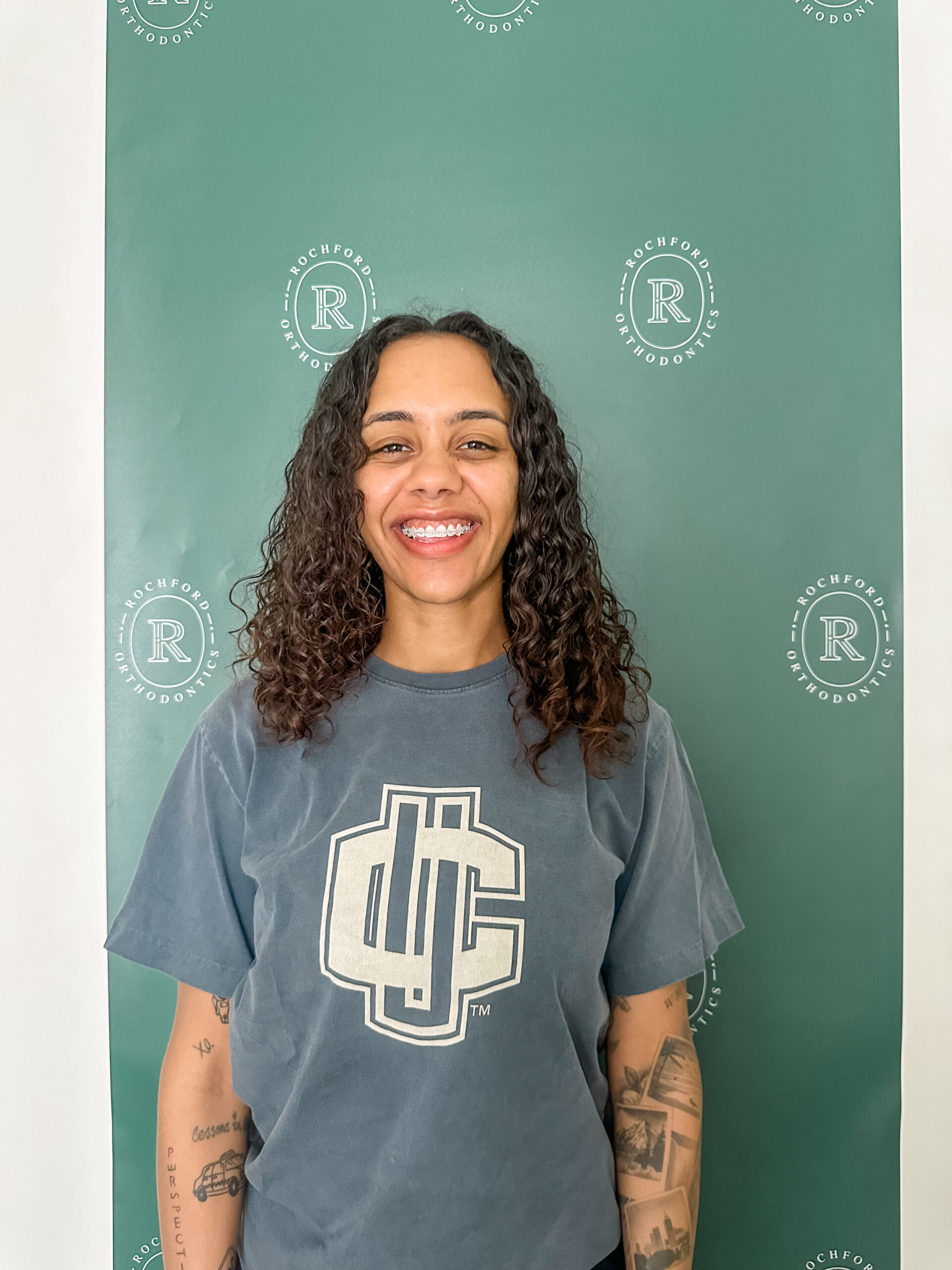 Female orthodontic patient smiling standing in front of a green wall.