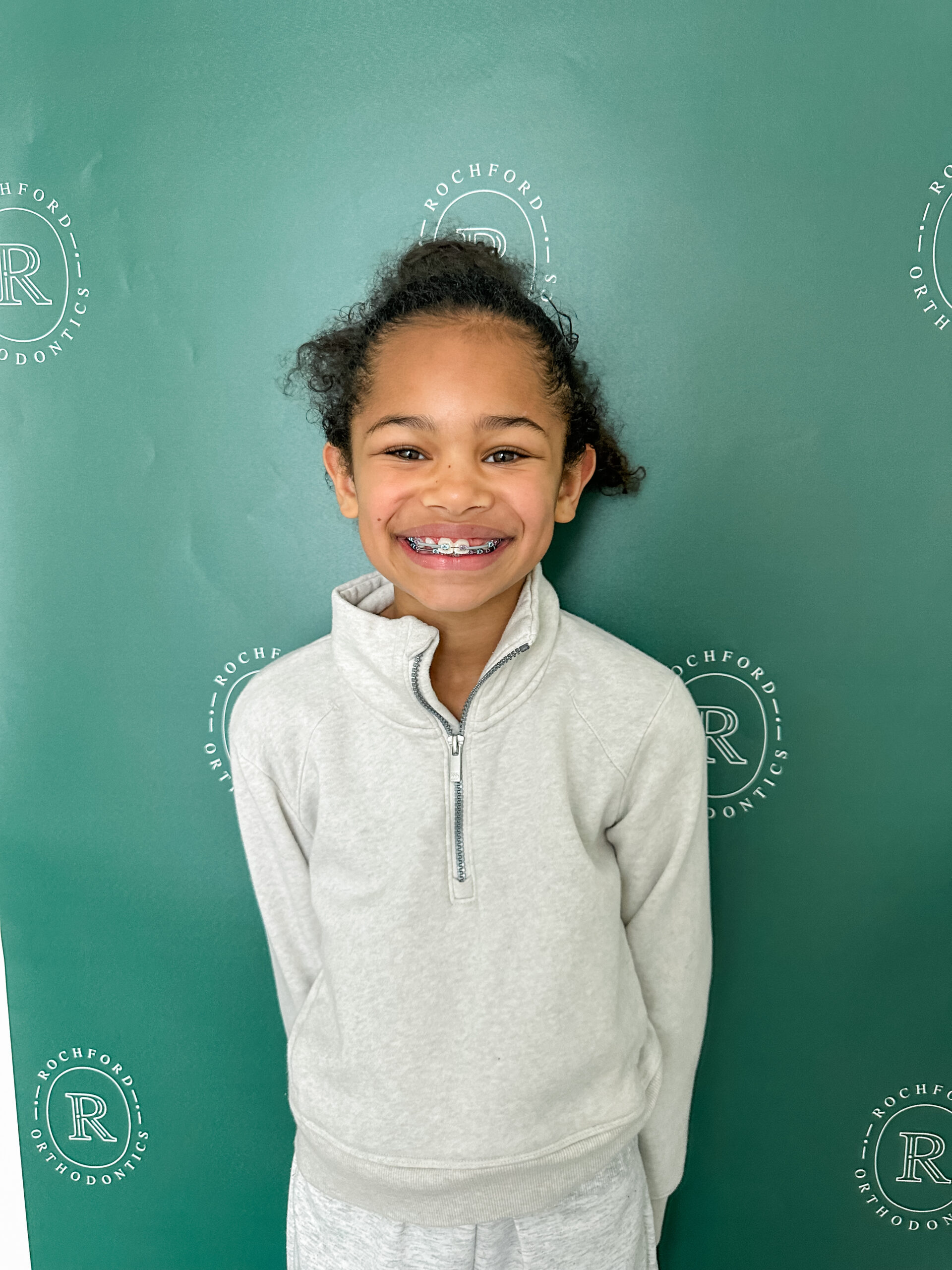 Little girls with braces, smiling, standing in front of a banner at an orthodontic office.